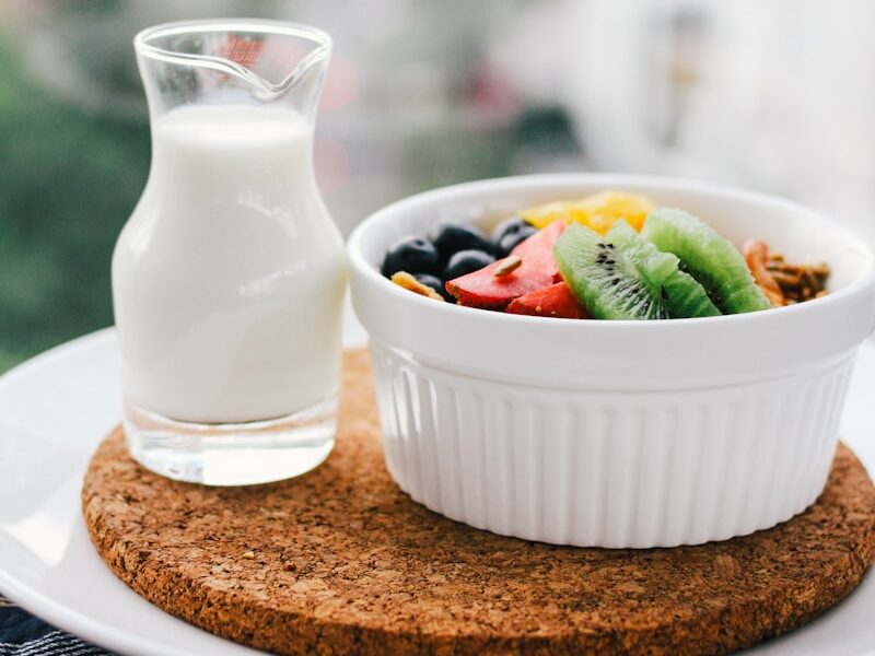fruit salad inside bowl beside glass of milk on brown board